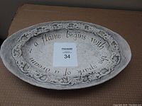 Top view of the oval raised cement platter showing the floral border and inscribed quote.