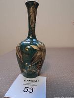 Green and gold pottery bud vase showing full front profile with floral gold decoration on deep green background.