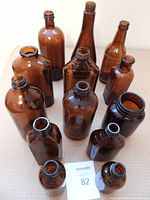 Top-down view showing all 13 brown glass bottles of various shapes and sizes arranged on a surface, highlighting the different neck openings and body shapes.