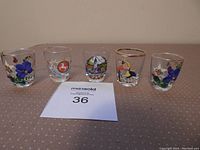 Five hand-painted clear shot glasses with varied detailed designs and colors displayed in a row