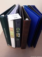 Front view of six 1.5-inch three-ring binders in different colors standing upright side by side, showing spine labeling and condition.