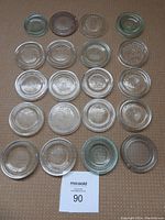 Overview of 20 vintage glass Mason jar lids laid flat, showing embossed Crown logos and starburst patterns in clear and green-tinted glass.