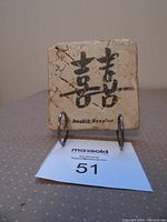 Front view of square stone tile with Japanese characters and English text 'double happiness'. Tile is supported by the aluminum stand and placed on a fabric surface.
