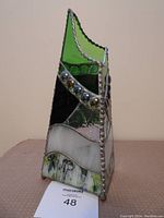 Front left angle showing green top, dark green glass, multi-colored beads, white band and base with green textured pattern.