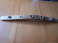 Long curved wood candleholder with five small silver metal cups for holding candles, resting on a wooden table surface.