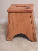 Side view of wooden step stool showing natural wood finish, visible knots, cracks at base, and arched cutout.