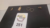 Five jewelry pieces displayed on black mat: treble clef pendant, rectangular plaque pendant, two hoops, pair of studs