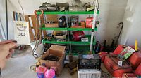 Shelving and floor area showing various automotive tools, parts in boxes, battery charger, cans, and other equipment in a garage.