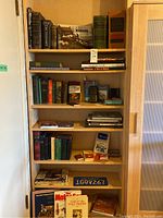 Full view of wooden bookshelf holding several shelves of books and some miscellaneous papers and items.