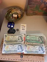 Overview of Canadian one dollar bills displayed on flat surface with coins in holder and shell nearby