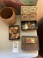 Photo showing containers of coins, ceramic crock, currency bills, carved wooden box with vintage toy car on top.