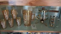 Vintage carnival glass pitcher and matching drinking glasses on shelf, alongside glass coffee carafe with metal heating stand and wooden handle.