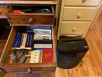 Drawer open showing various pens in cases, stapler, stamps, notes book, and black Aurora paper shredder next to drawer.