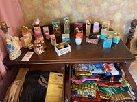 Wide shot showing perfume bottles arranged on top of a wooden surface with gloves and folded scarves/handkerchiefs in drawers below.