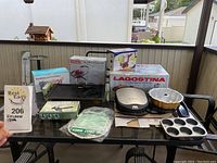 Wide shot of all kitchen items on glass table including roasting pan box, contact grill, bakeware and gloves.