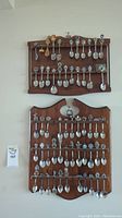 Full view of two wooden wall racks filled with decorative spoons showing varied themes and enamel accents.