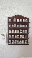 Full front view of the wooden display shelf mounted on wall, showing all 33 porcelain thimbles arranged on five rows.