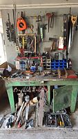 Green metal workbench with tools and pegboard showing assortment of hand tools and storage bins