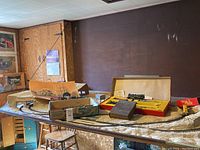 Wide view showing the complete scenic train set layout on a table with various boxes and model train pieces visible.