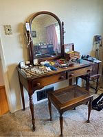 Front view of wooden vanity with large arched mirror and stool. Shows jewelry and small items on top but contents not included.