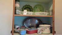 Wide shot showing a cabinet shelf with various vintage glass dishes, metal tray, and Pyrex casseroles.