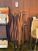 Full view of five walking canes leaning against wooden wall, showing size and finish variety.
