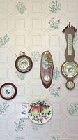 Photo showing wall with three round barometers, an elongated wooden weather instrument, and a decorative ceramic plate with fruit design.