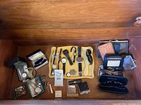 Wide view of the lot showing multiple wristwatches, wallets, vintage lighters, and small accessories laid out on a wooden surface and tray.
