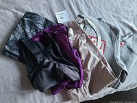 Photo of all five items folded: a patterned black/purple/lilac pieces, beige pant, and grey Canada hoodie