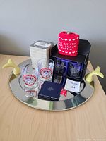 Serving tray with yellow whale-shaped handles holding various glasses, boxes, and a red beverage koozie. Items arranged for clear display.