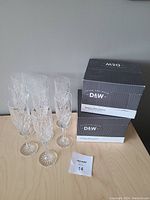 8 crystal champagne flutes arranged on a table with 2 boxes of stemless wine glasses in the background