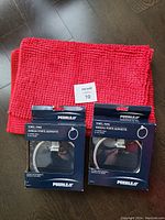 Two chrome towel rings still in box packaging side by side on top of a red textured bath mat.