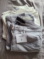 Two pairs of folded Calvin Klein jeans in grey and white, showing the front waist labels and tags.