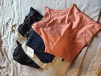 Stack of folded clothing including crop top, leggings, sweater dress, Bench dress, and hoodie, all gently used.