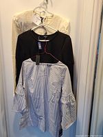 Three clothing items hung together: white textured top, black dress, and blue striped top
