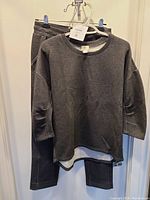 Full view of dark gray long-sleeve sweater and matching lounge pants hanging on clips.