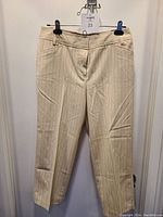 Off-white pinstripe dress pants hanging on black clips, showing full front view with faint crease and zipper fly.