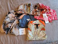 Six ladies casual clothing items including Dalia tunic with tags, patterned tops and J.Crew chambray dress displayed on brown fabric surface