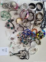 Collection of assorted bangles, bracelets, rings, and necklaces spread out on a white surface, showing different colors, styles, and designs