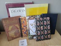 Lot of 7 assorted notebooks, planners, and drawing pads shown on table, some new in plastic and some used.