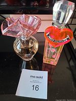 Two perfume bottles side by side on black surface with MaxSold lot number.