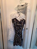 Three dresses hanging on white hangers on door: white Ann Taylor eyelet dress, black floral Monteau dress, and gray AllSaints slip dress
