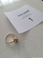 Photo of the gold ring placed on a surface showing the ring and the lot number tag.