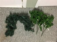 Top-down photo of dark green artificial fir garland on left and four upright fir florist picks on right against carpet background.