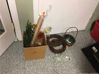 Shows bulk lot of various florist supplies including artificial greenery, decorative balls, a metallic reindeer figure, grapevine wreath frames, a basket, and clear plastic covers.
