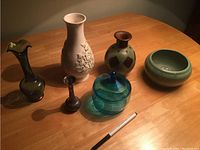 Six assorted vases and containers displayed on wooden surface.