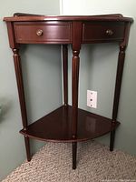 Front angle view of the dark wooden corner table showing two small drawers with brass knobs and four rounded carved legs.