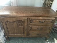 Front view of French carved oak antique cabinet showing the door and three drawers with carved details and brass handles.