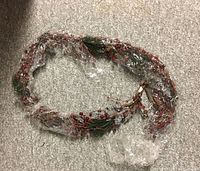 Full view of the holiday garland wrapped in plastic showing the mixed elements of pine, berries, cones, and ice.