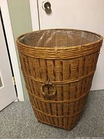 Front view of tall wicker laundry basket showing weaving pattern, lid, and plastic liner inside
